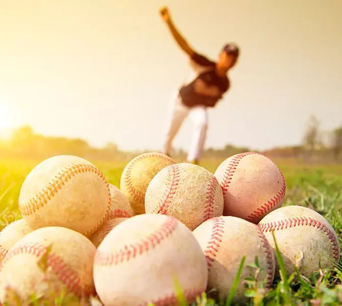 A man standing in the grass with several baseball balls.